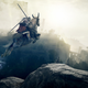 A fantasy horse with horns jumps in mid-air between two rocky outcroppings.